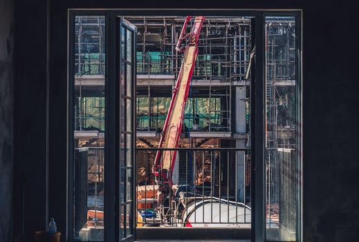 Vertical view from window. Technical modern telescopic self erection crane. Concrete multi-storey new house residential building construction process using formwork. Industry, real estate investment