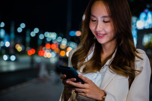 Business woman using mobile phone walking through night city street while waiting car to pick up home, Beautiful young smiling female texting work on smartphone, social media