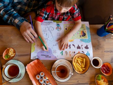 a child with his father in a restaurant draws a coloring book, waiting for cooking