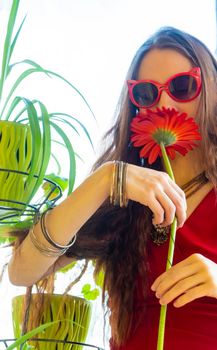 girl in a red dress and funny sunglasses holds a red gerbera flower