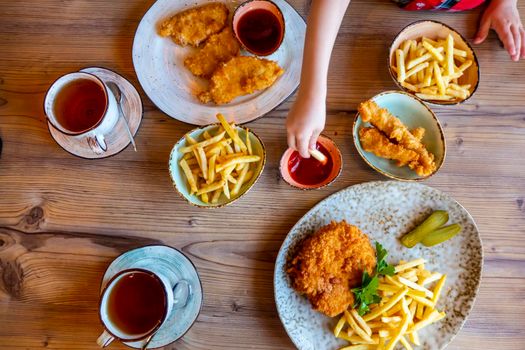 Children and man hands Picking French Fries on wood table in restaurant. French fries with ketchup on wooden background. High quality photo