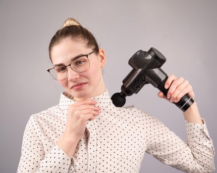 A caucasian woman uses a massager gun for pain in the muscles of her back and shoulders