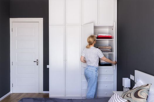 a woman stands with her back and looks into the closet, in which she put things in order. general plan, copy space. The concept of space organization, mess