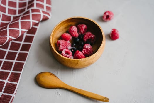 Wooden bowl with berries. Frozen raspberries and black currants.
