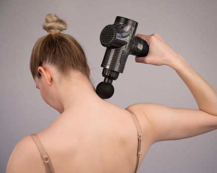 Caucasian woman giving herself a back massage with a gun