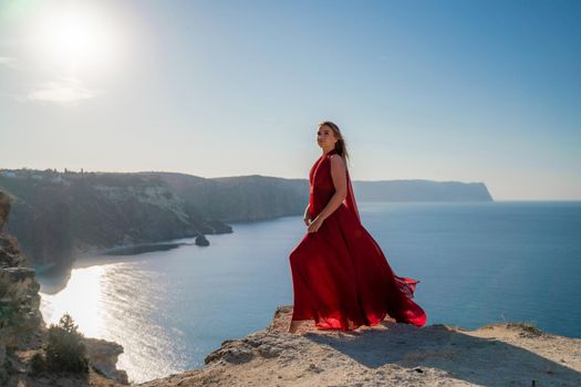 A woman in a red flying dress fluttering in the wind, against the backdrop of the sea