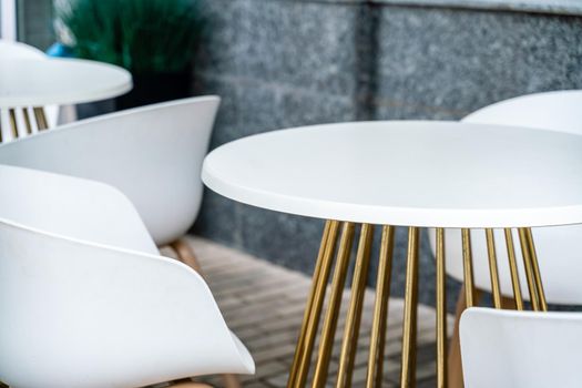 Street cafe with white chairs, green foliage around. Without people, tourism, travel