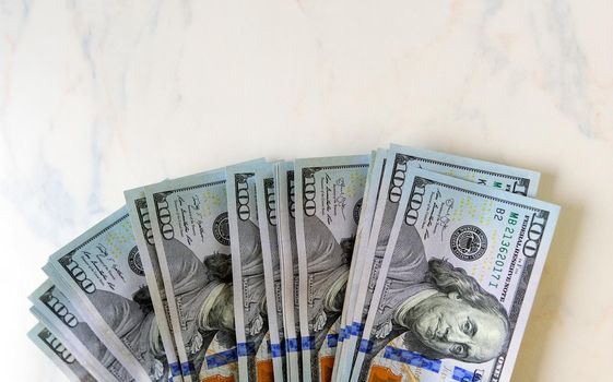 a stack of one hundred dollar bills lie on a marble table