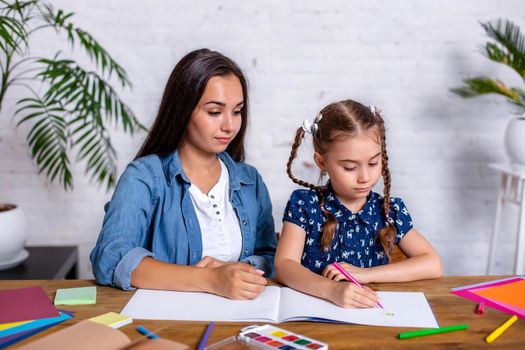 Happy family mother and daughter together draw with markers. Woman helps child girl.