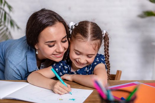 Happy family mother and daughter together draw with markers. Woman helps child girl.