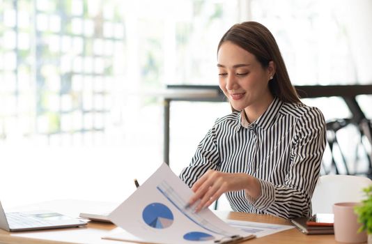 Beautiful Asian businesswoman analyzes charts using laptop calculator at the office..