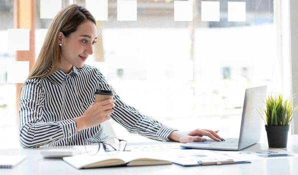 Beautiful young asian woman sitting at coffee shop using laptop. Happy young businesswoman sitting at table in cafe with tab top computer..