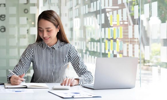 Beautiful Asian businesswoman analyzes charts using laptop calculator at the office..