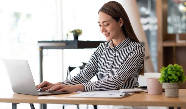 Charming asian businesswoman sitting working on laptop in office..