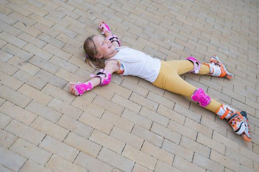 Little girl learns to roller skate and falls. View from above.