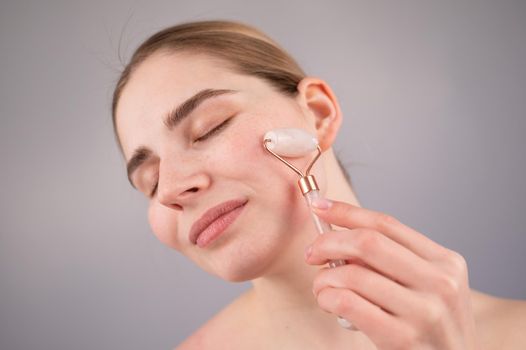 Close-up portrait of a woman using a quartz roller massager on her cheek for an alternative anti-aging