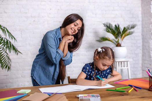 Happy family mother and daughter together draw with markers. Woman helps child girl.