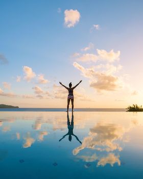 Young women with hands up at Saint Lucia Caribbean, men at infinity pool during sunset. women in bikini at the pool