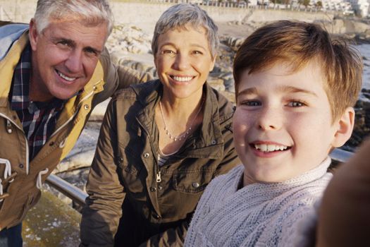 Great smiles run in the family. an adorable little boy taking a selfie with his grandparents at the beach