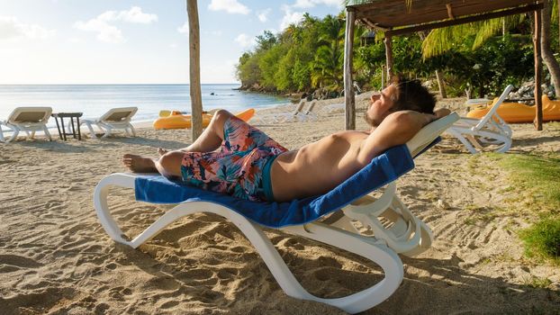 Young men sunbathing tanning in the evening sun on a beach chair in Saint Lucia Caribbean. caucasian men sunbathing during sunset