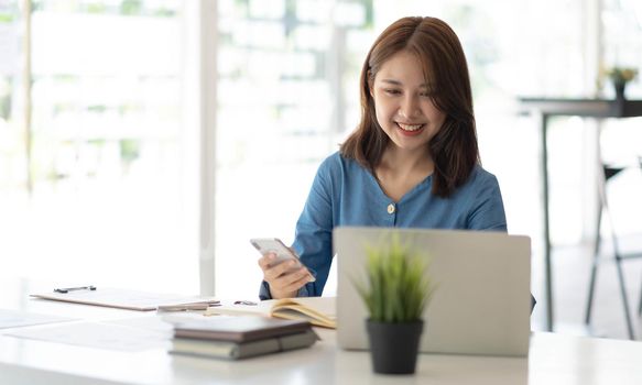 Asian businesswoman in formal suit in office happy and cheerful during using smartphone and working.