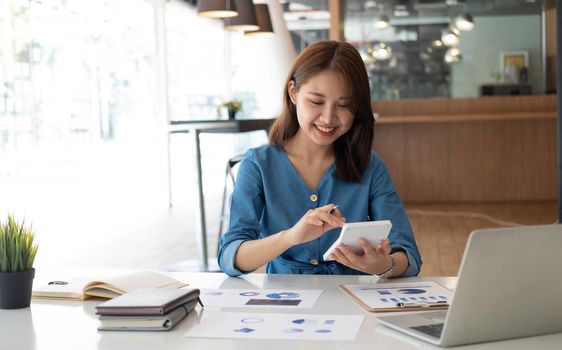 Portrait of asian business woman paying bills online with laptop in office. Beautiful girl with computer and chequebook, happy paying bills. Startup business financial calculate account concept.