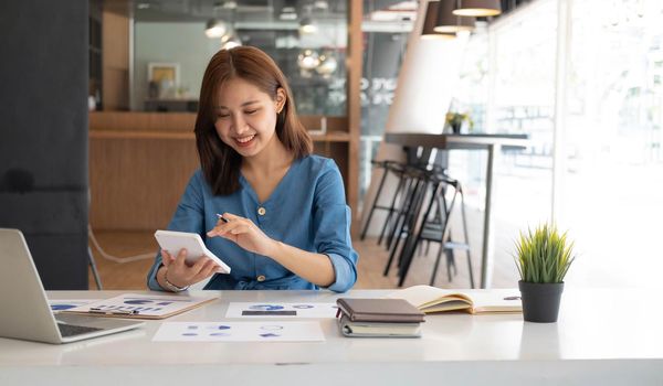 Young Asian businesswoman using a calculator to calculate business principles. Accounting statistics concept at the office..