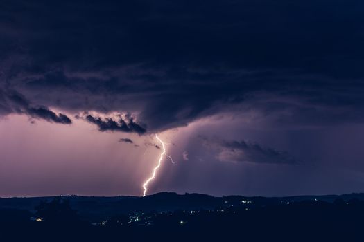 Night landscape on a background of thunderstorms. Rural silhouette and clouds with lightning flashes