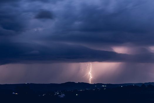 Night landscape on a background of thunderstorms. Rural silhouette and clouds with lightning flashes