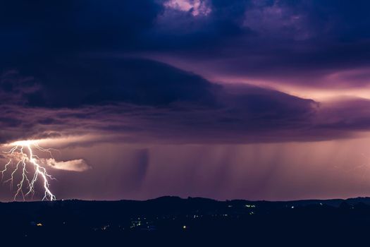 Night landscape on a background of thunderstorms. Rural silhouette and clouds with lightning flashes