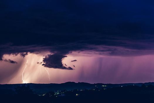 Night landscape on a background of thunderstorms. Rural silhouette and clouds with lightning flashes