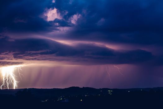 Night landscape on a background of thunderstorms. Rural silhouette and clouds with lightning flashes