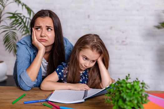 Mother becoming frustrated with daughter whilst doing homework sitting at the table at home in learning difficulties homework. Parenting and education concept