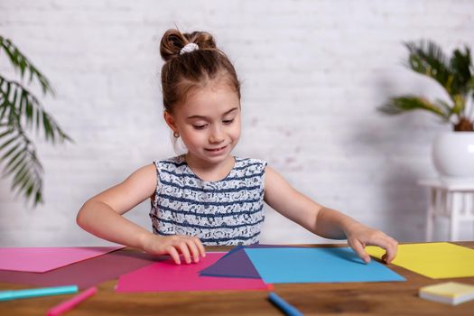 Cute little girl at the table with the colored paper