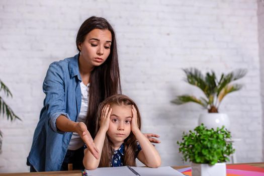 Mother becoming frustrated with daughter whilst doing homework sitting at the table at home in learning difficulties homework. Parenting and education concept