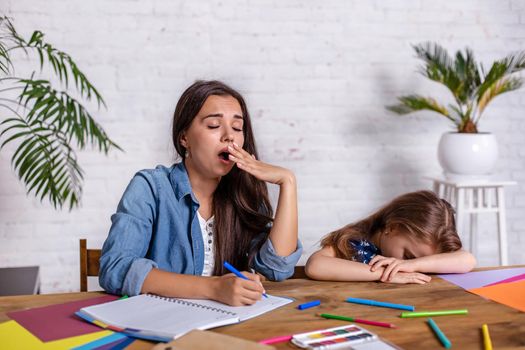 Cute little girl sleeping while her mother looking tired, helping her with studying. Home education