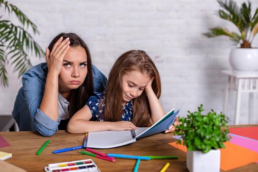 Mother becoming frustrated with daughter whilst doing homework sitting at the table at home in learning difficulties homework. Parenting and education concept