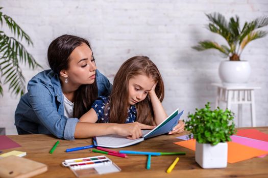 Mother becoming frustrated with daughter whilst doing homework sitting at the table at home in learning difficulties homework. Parenting and education concept