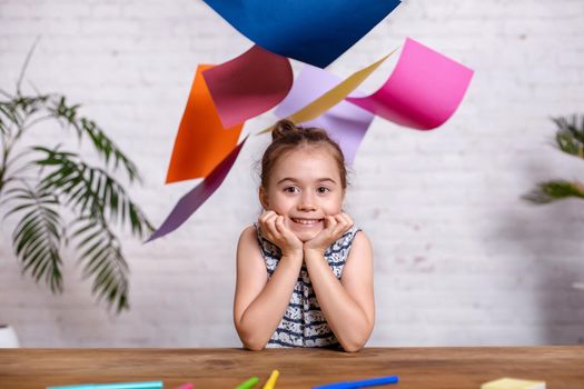 Cute little girl at the table with the colored paper