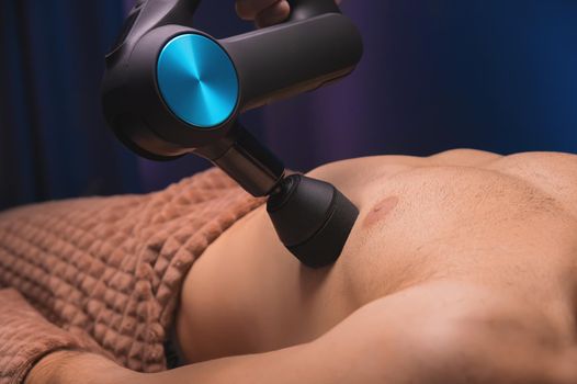 Therapist treats an athlete's chest injury with a massage gun, percussion massager.