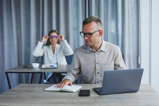 Portrait of a cheerful man, IT professional, working with a modern laptop, sitting at a table and smiling at the camera during a break, a happy human programmer in vision correction glasses
