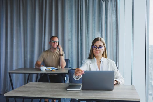 Woman with glasses at the table while working with colleagues in the office. Concept of modern successful business people. Man and woman sitting at wooden tables