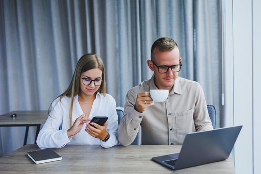 Young business team, male and female colleagues talking at work, discussing a new project with a laptop, young executives having a friendly conversation, collaborating in teamwork in the office