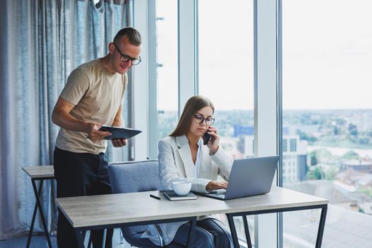 A young woman at a laptop in glasses sits at a table, having a corporate business meeting with colleagues in a modern office. business career concept. Free space, selective focus