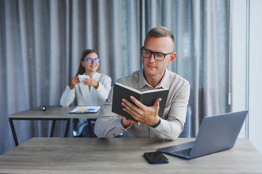 Portrait of a cheerful man, IT professional, working with a modern laptop, sitting at a table and smiling at the camera during a break, a happy human programmer in vision correction glasses