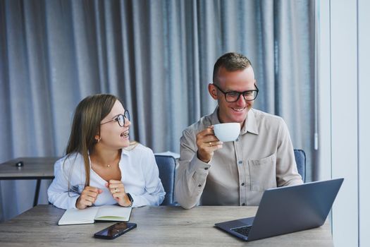 Young business team, male and female colleagues talking at work, discussing a new project with a laptop, young executives having a friendly conversation, collaborating in teamwork in the office