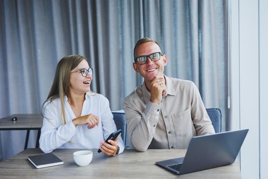 Young business team, male and female colleagues talking at work, discussing a new project with a laptop, young executives having a friendly conversation, collaborating in teamwork in the office