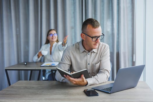 Portrait of a cheerful man, IT professional, working with a modern laptop, sitting at a table and smiling at the camera during a break, a happy human programmer in vision correction glasses