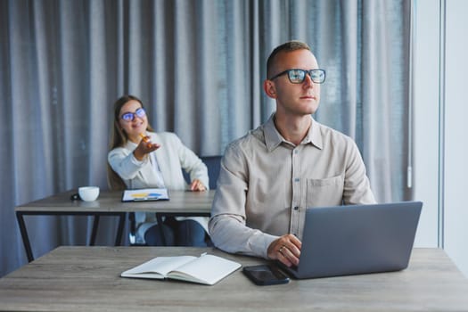 Portrait of a cheerful man, IT professional, working with a modern laptop, sitting at a table and smiling at the camera during a break, a happy human programmer in vision correction glasses