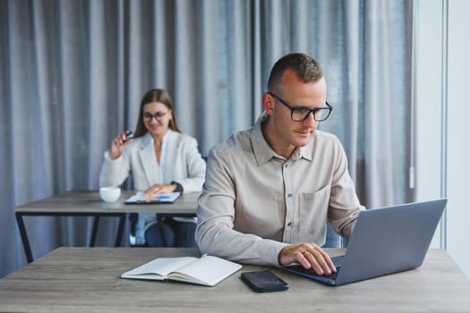 Portrait of a cheerful man, IT professional, working with a modern laptop, sitting at a table and smiling at the camera during a break, a happy human programmer in vision correction glasses